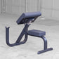 Navy blue preacher curl bench with padded seat and back support on concrete floor in gym setting