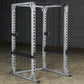 White metal power rack with adjustable holes and black safety bars, displayed in garage setting