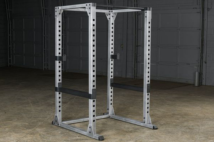 White metal power rack with adjustable holes and black safety bars, displayed in garage setting