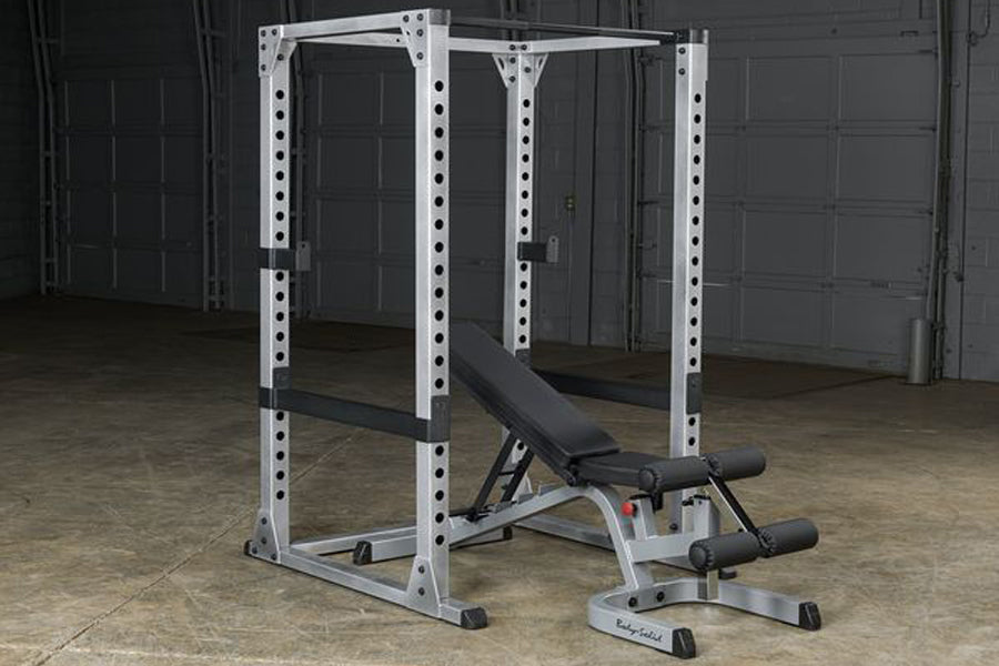White metal power rack with perforated uprights and adjustable weight bench with black padding in garage setting