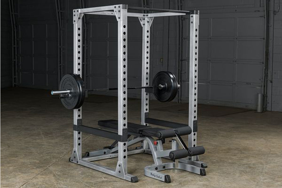 White and black power squat rack with barbell and weight plates in garage setting