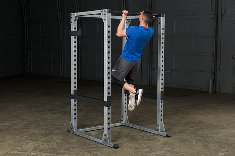 Man in blue shirt performing pull-up on silver power rack with black safety bars in gym setting
