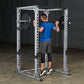 White and black steel power rack with man in blue shirt performing squat exercise, adjustable safety bars and weight loaded b