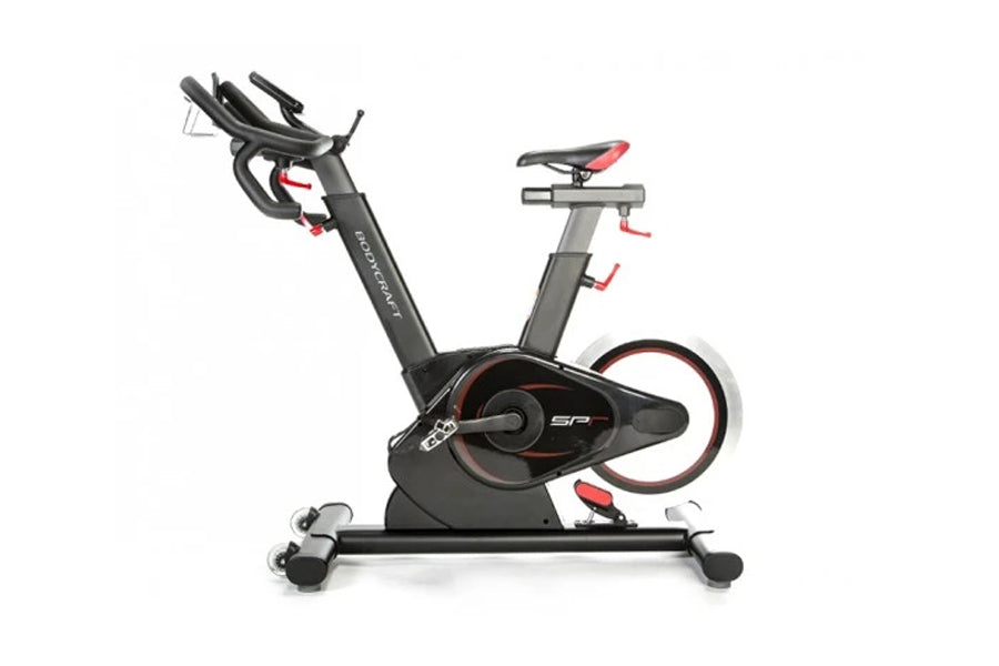 Black and red stationary indoor cycling bike with adjustable handlebars, padded seat, and weighted flywheel on white backgrou