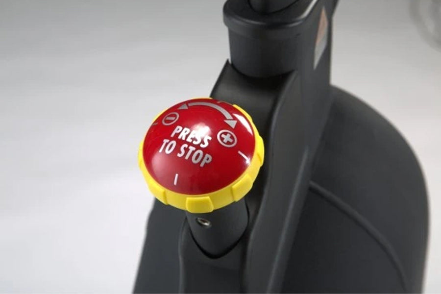 Red and yellow "Press to Stop" brake button mounted on black indoor cycle handlebar