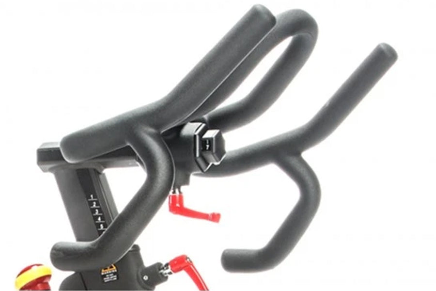 Black stationary indoor cycling bike with padded handlebars and red accent details on white background