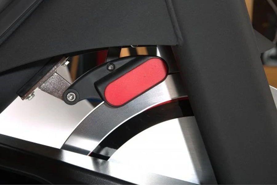 Stationary bike resistance pad with red cushion and black metal lever adjustment mechanism mounted on chrome frame