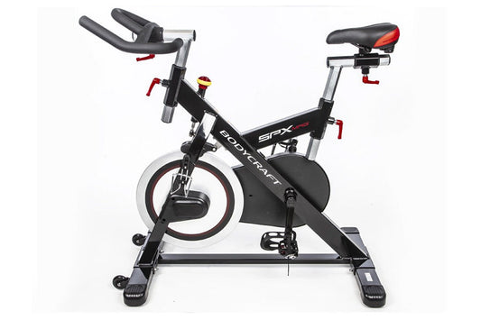 Black and red indoor training cycle with curved handlebars, padded seat, and stabilizer base on white background
