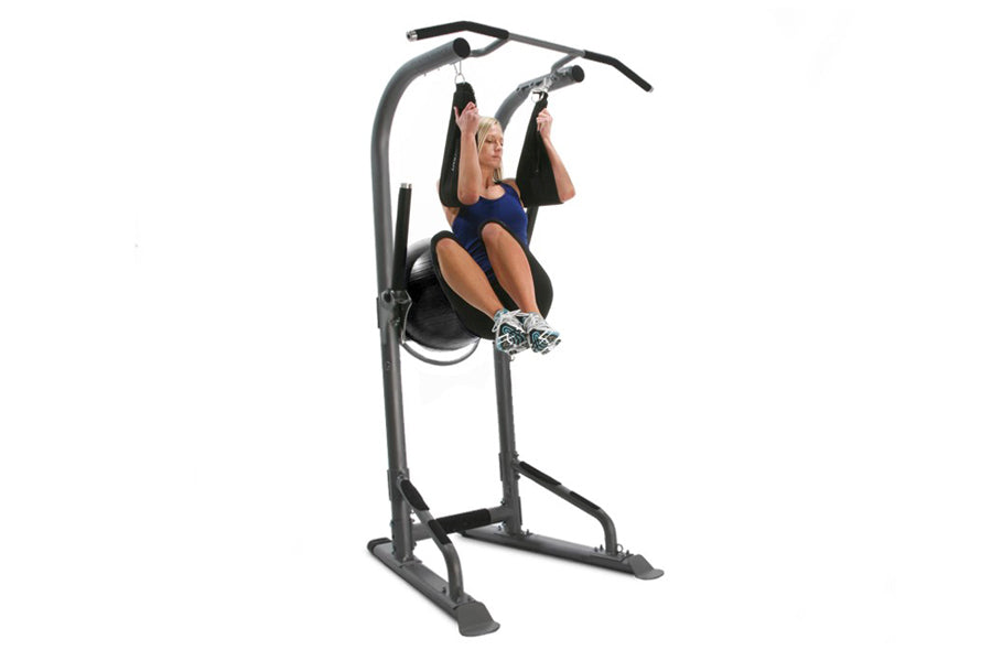 Woman using gray and black vertical training tower with pull-up bar and leg raise station on white background