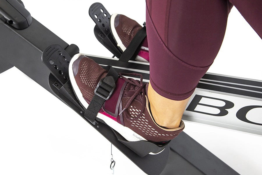 Burgundy leggings and brown perforated water shoes worn on rowing machine footplate, white socks visible