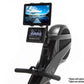 Black and gray upright stationary bike with digital console displaying metrics, tablet holder mounted on handlebar showing la