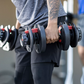 Man holding pair of black adjustable dumbbells with red handles in gym setting