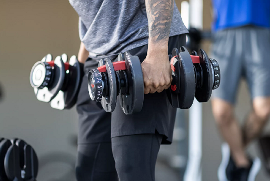 Man holding pair of black adjustable dumbbells with red handles in gym setting