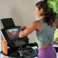 Woman wearing sage green sleeveless tank and purple leggings running on black BowFlex treadmill with digital display, orange 