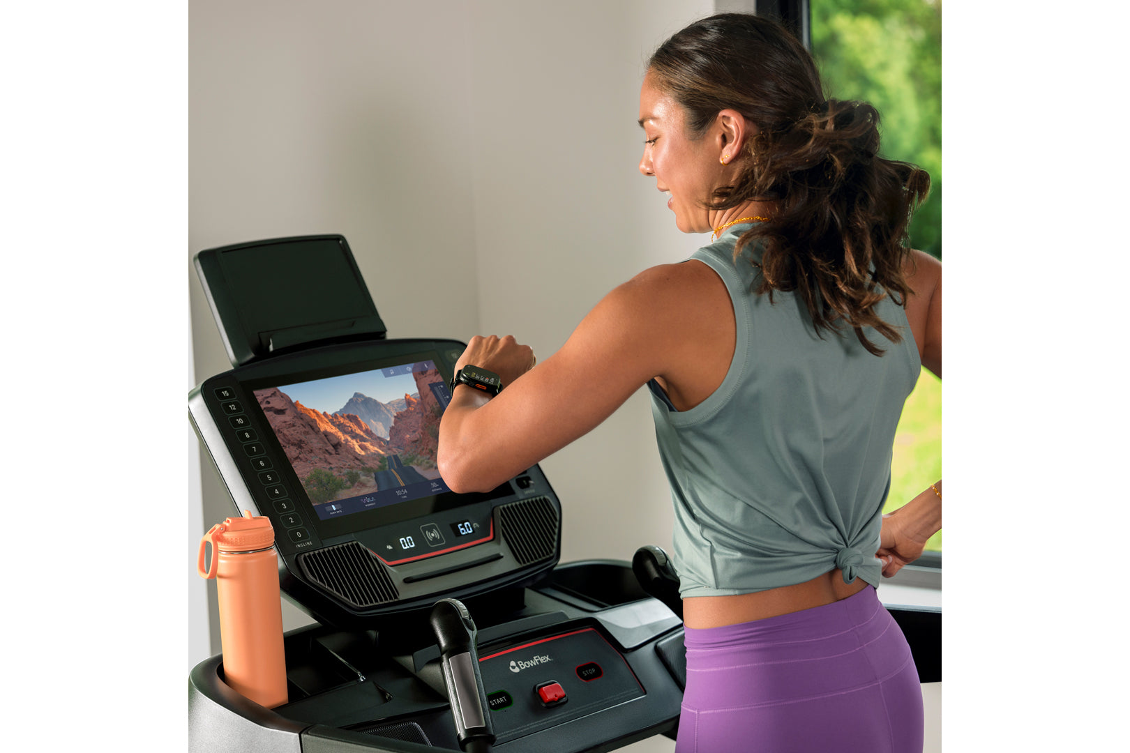 Woman wearing sage green sleeveless tank and purple leggings running on black BowFlex treadmill with digital display, orange 