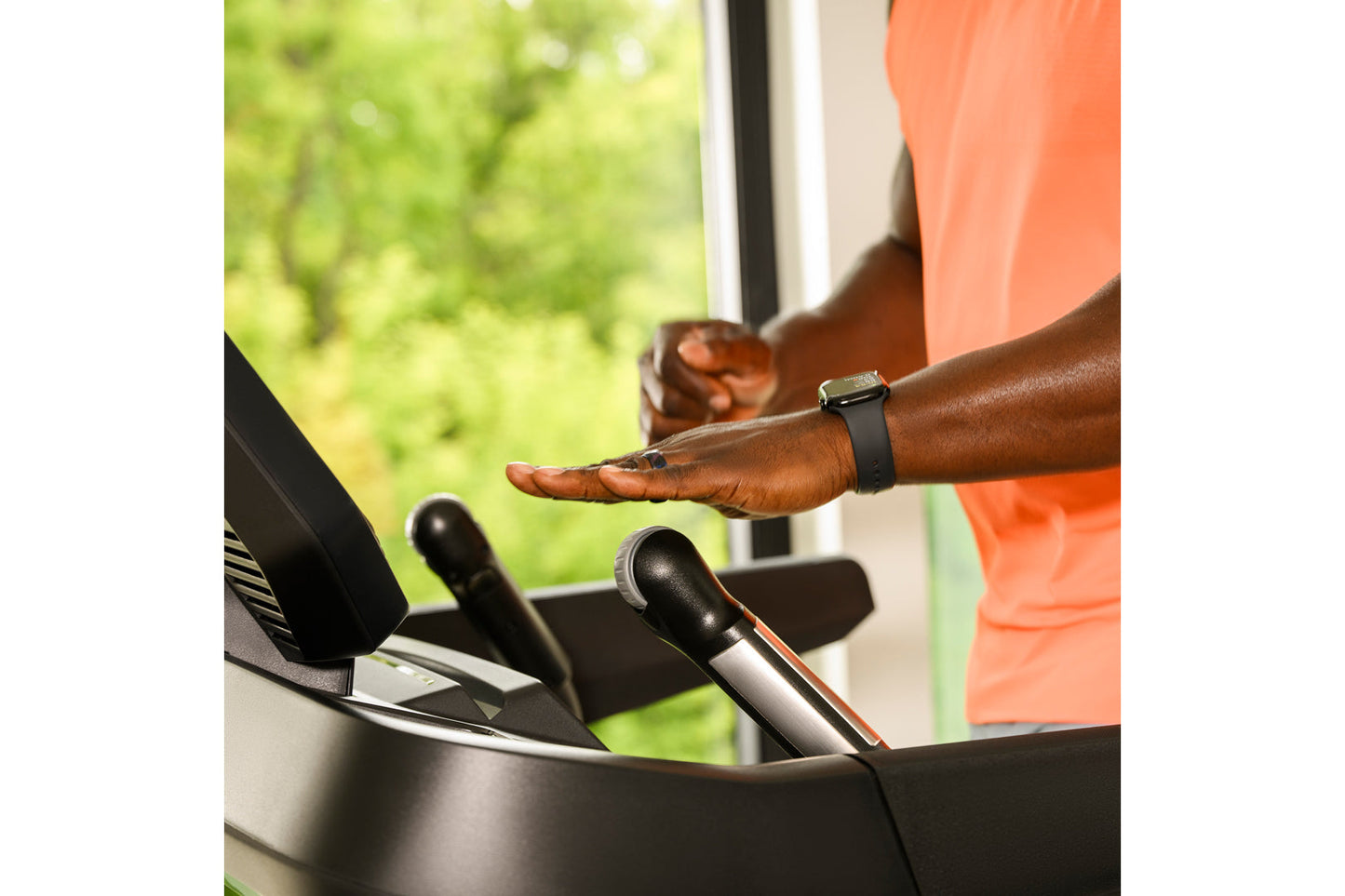 Person wearing orange shirt and black smartwatch using Bowflex T16 treadmill with hand on console near window