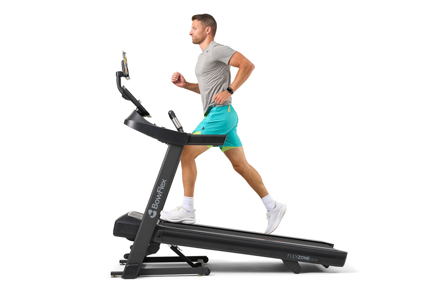 Man running on black Bowflex T6 treadmill, wearing gray sleeveless shirt and turquoise shorts with white sneakers, on white b