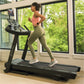 Woman wearing coral tank top and sage green leggings running on black Bowflex treadmill in bright gym with large windows