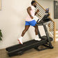 Man wearing light pink sleeveless tank top and blue shorts running on black Bowflex treadmill in home gym setting