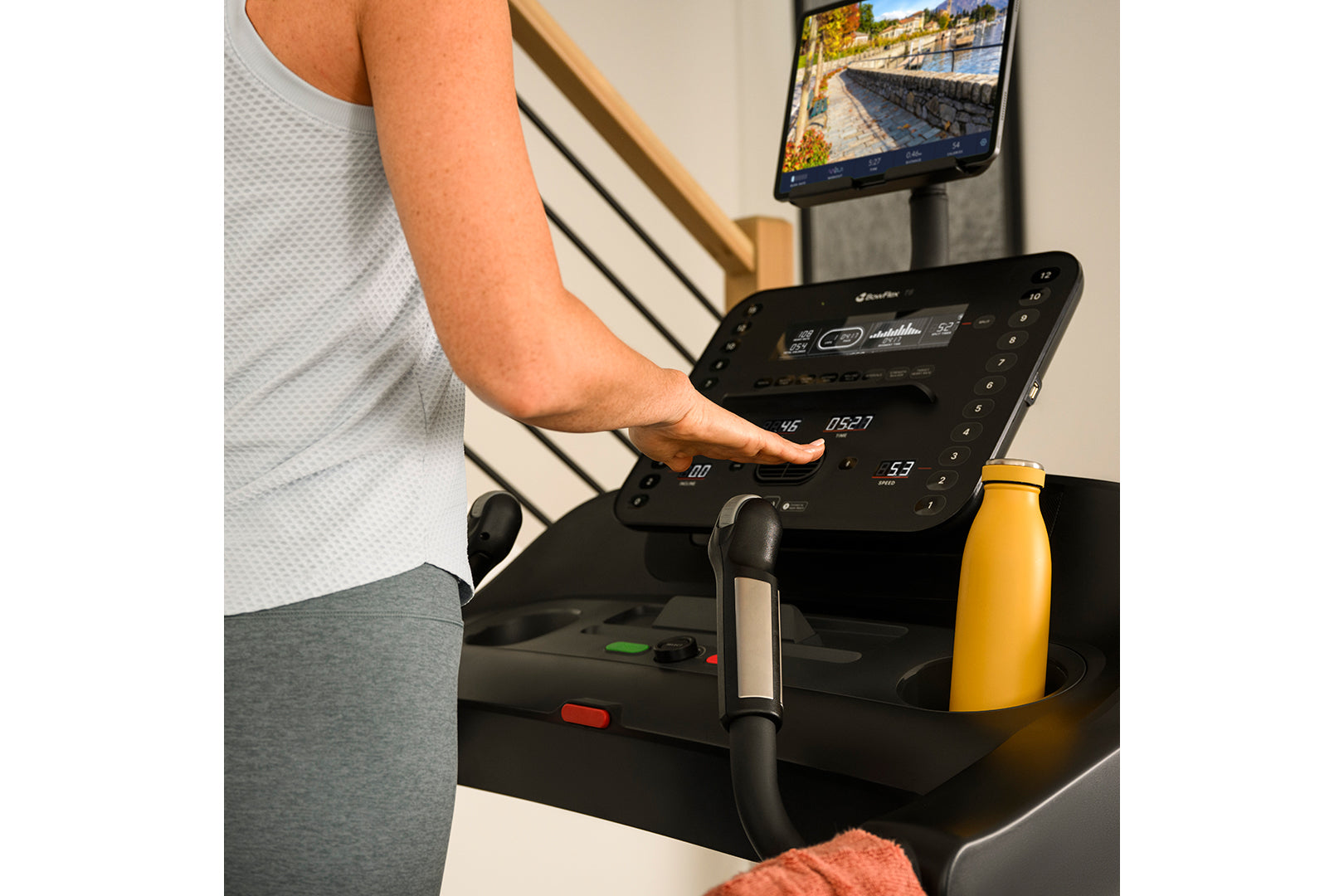 Person in light gray shirt using black Bowflex T6 treadmill console with screen displaying workout data, yellow water bottle 