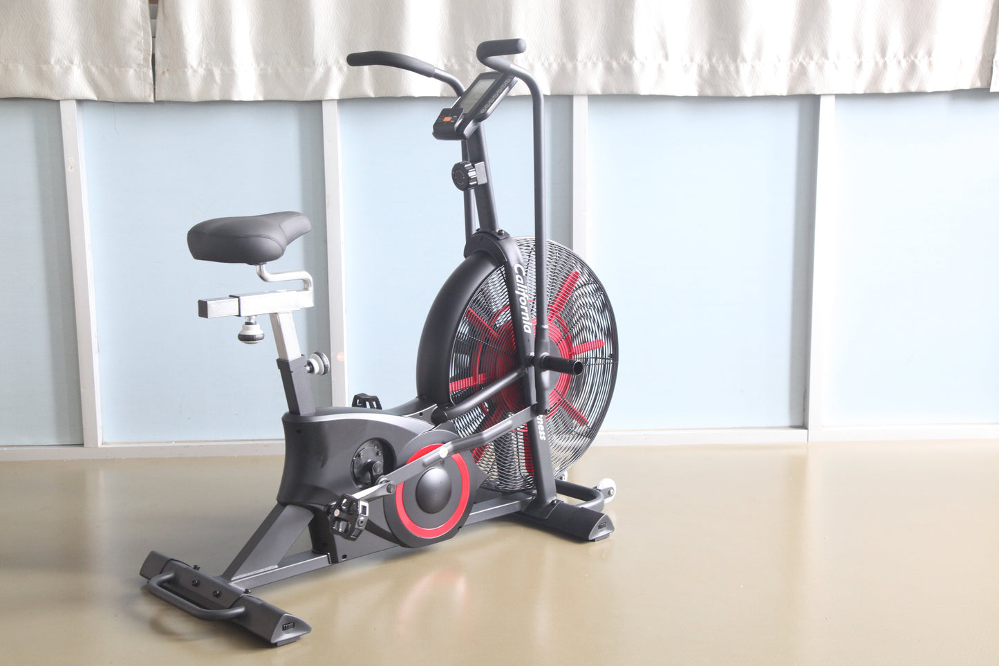 Black and red stationary air exercise bike with large fan wheel, digital display, and padded seat, on light background