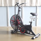 Black and red stationary air exercise bike with large fan wheel, curved handlebars, and padded seat on wood floor