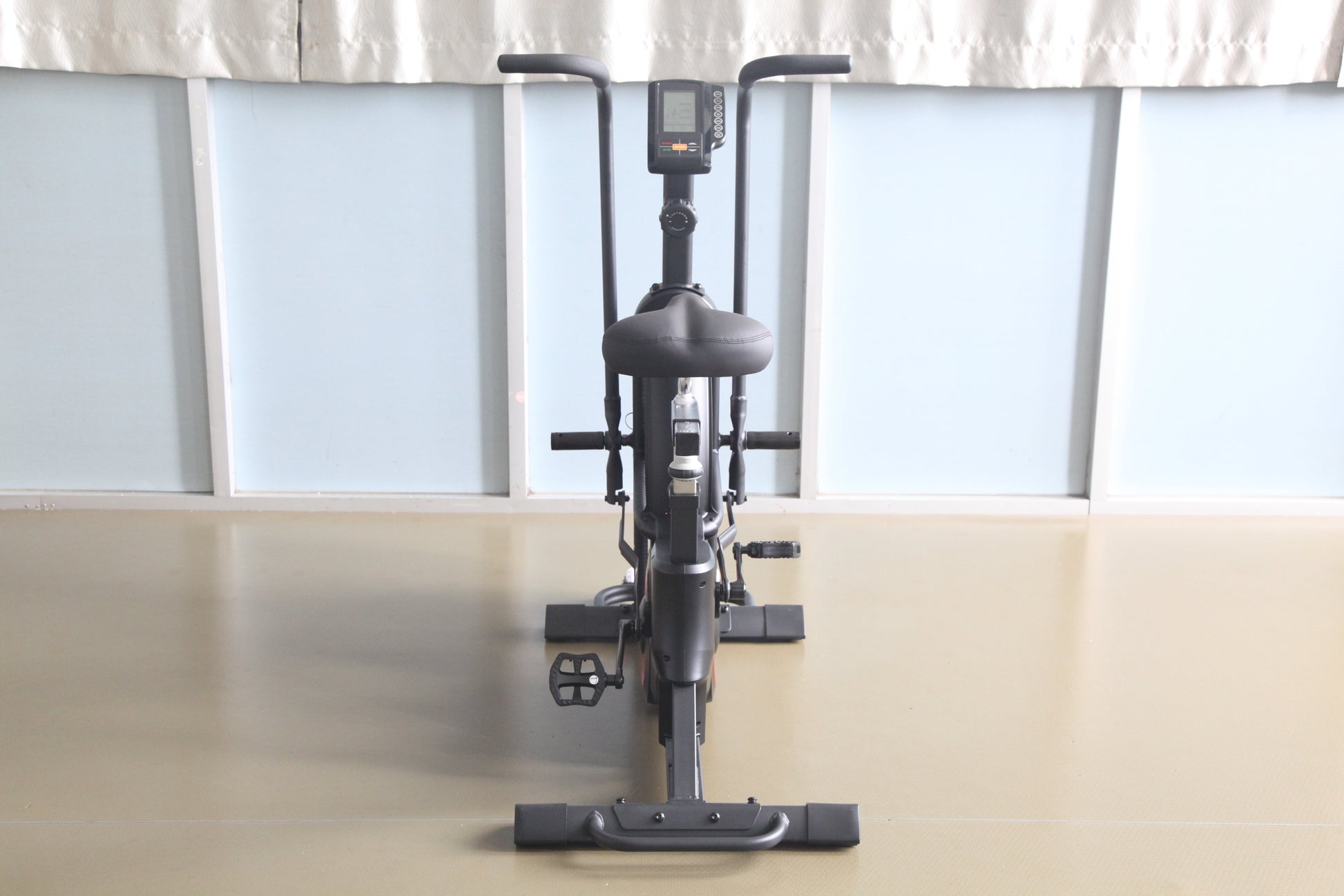 Black upright exercise bike with digital display console, padded seat, handlebars, and pedals with foot straps, front view on