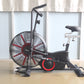 Black and red air exercise bike with large fan wheel, upright handlebar, and padded seat on wood floor