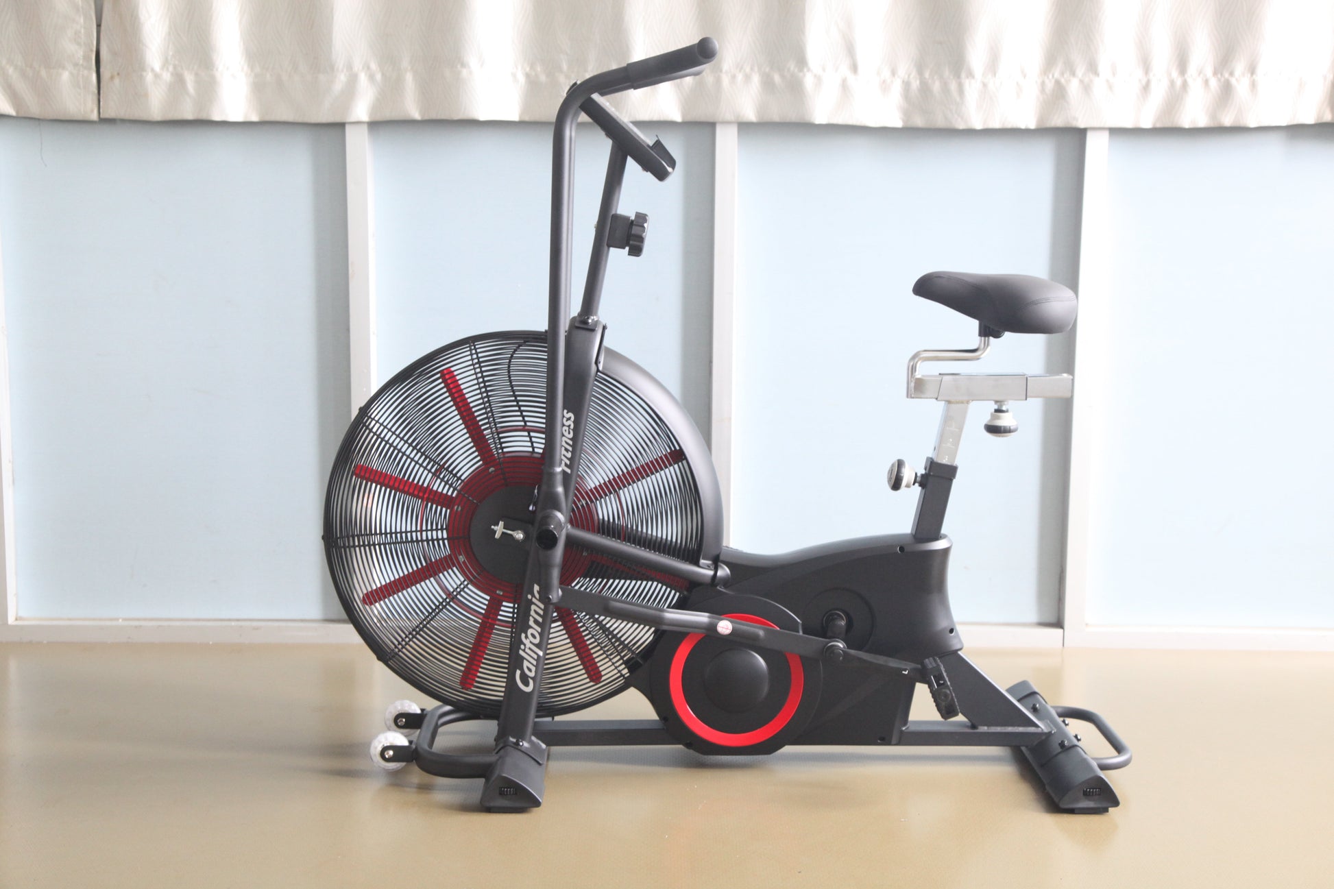 Black and red air exercise bike with large fan wheel, upright handlebar, and padded seat on wood floor