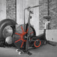 Black and red air exercise bike with large fan wheel, seat, and handlebars in industrial gym setting with tire and equipment
