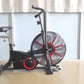 Black and red air resistance exercise bike with large fan wheel and padded seat on white background