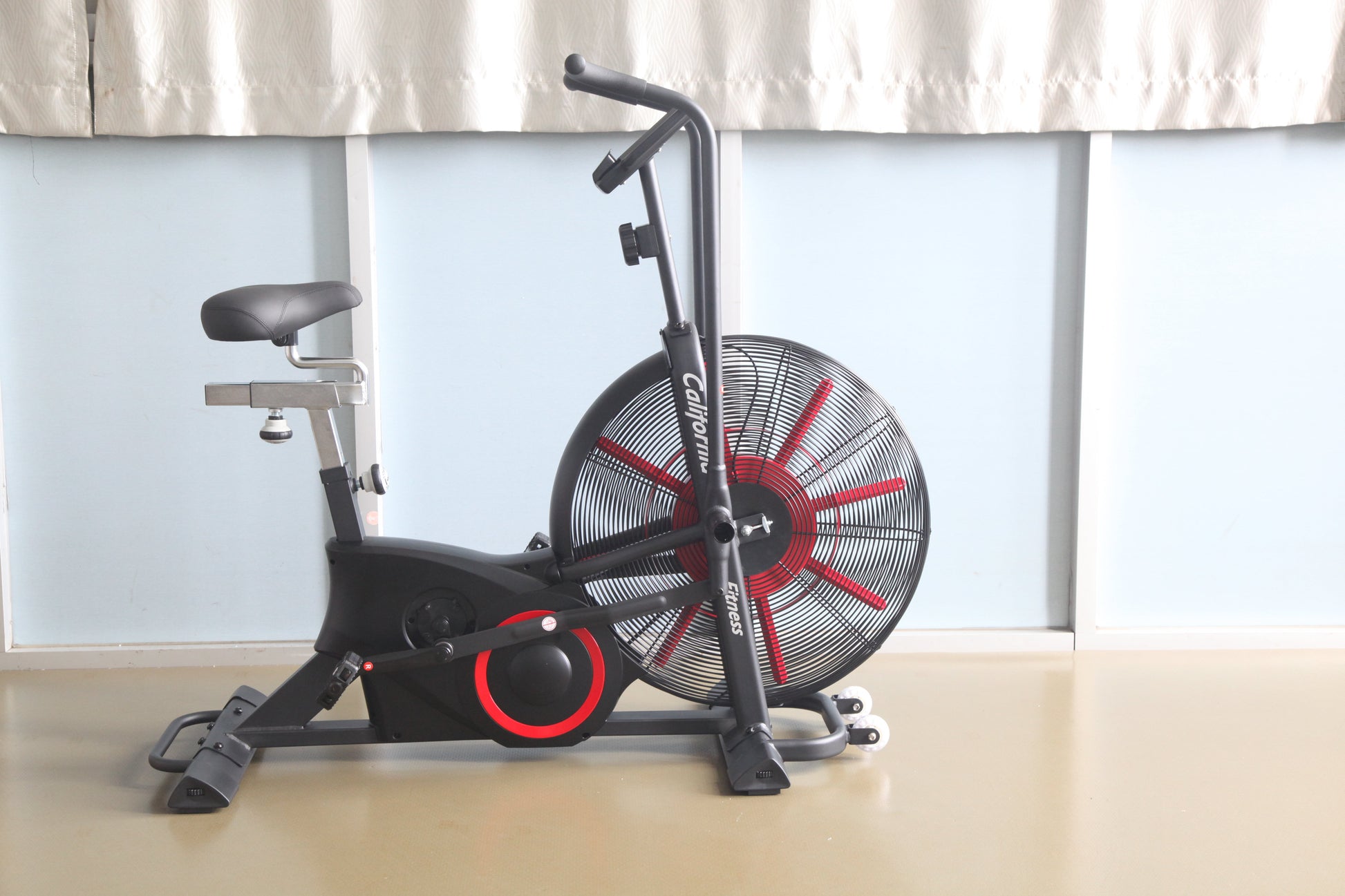 Black and red air resistance exercise bike with large fan wheel and padded seat on white background