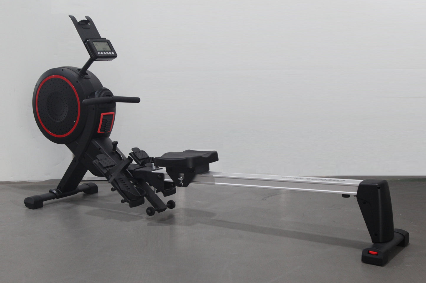 Black and red rowing machine with digital display monitor, foot pedals, and sliding seat on metal rail, on gray background