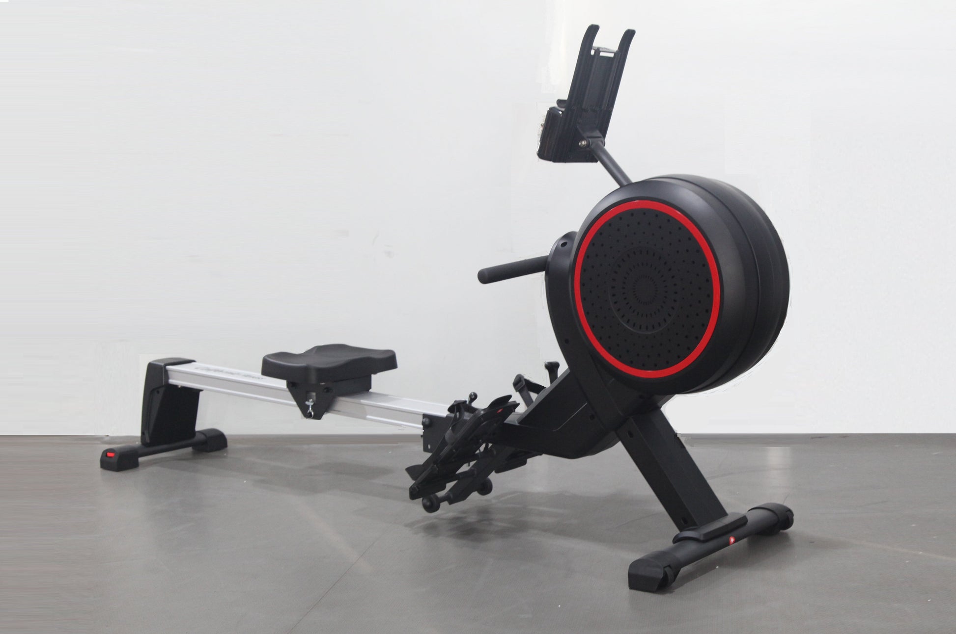 Black rowing machine with red accent ring on flywheel, tablet holder, and silver rail on gray floor