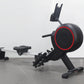 Black and red stationary rowing machine with aluminum rail, adjustable seat, foot pedals, and phone holder on white backgroun