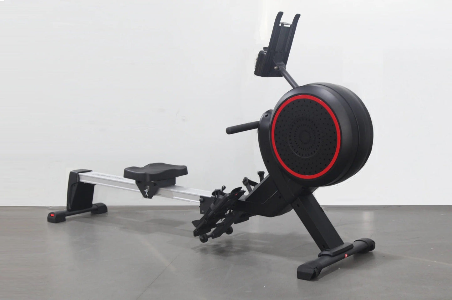 Black and red stationary rowing machine with aluminum rail, adjustable seat, foot pedals, and phone holder on white backgroun