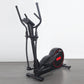 Black and red elliptical cross-trainer with dual handles and foot pedals on gray floor, white background