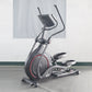 Black and gray stationary elliptical trainer with red accent trim and dual handle bars, displayed on concrete floor