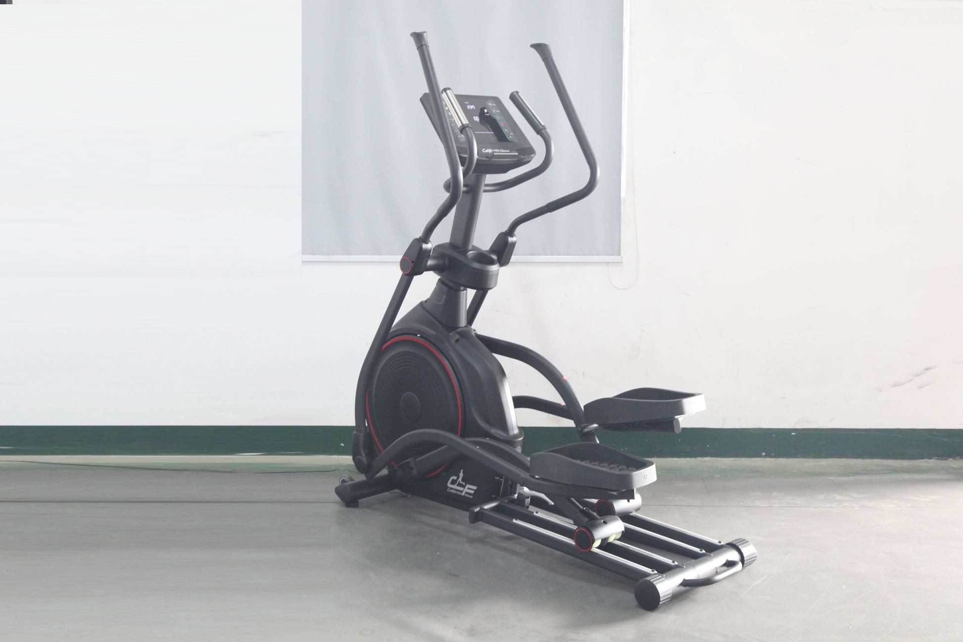 Black elliptical incline trainer with red accents, curved handles, digital display console, and extended footplate on gray fl