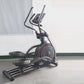 Black and red elliptical incline trainer with dual curved handles and digital display on concrete floor against white wall