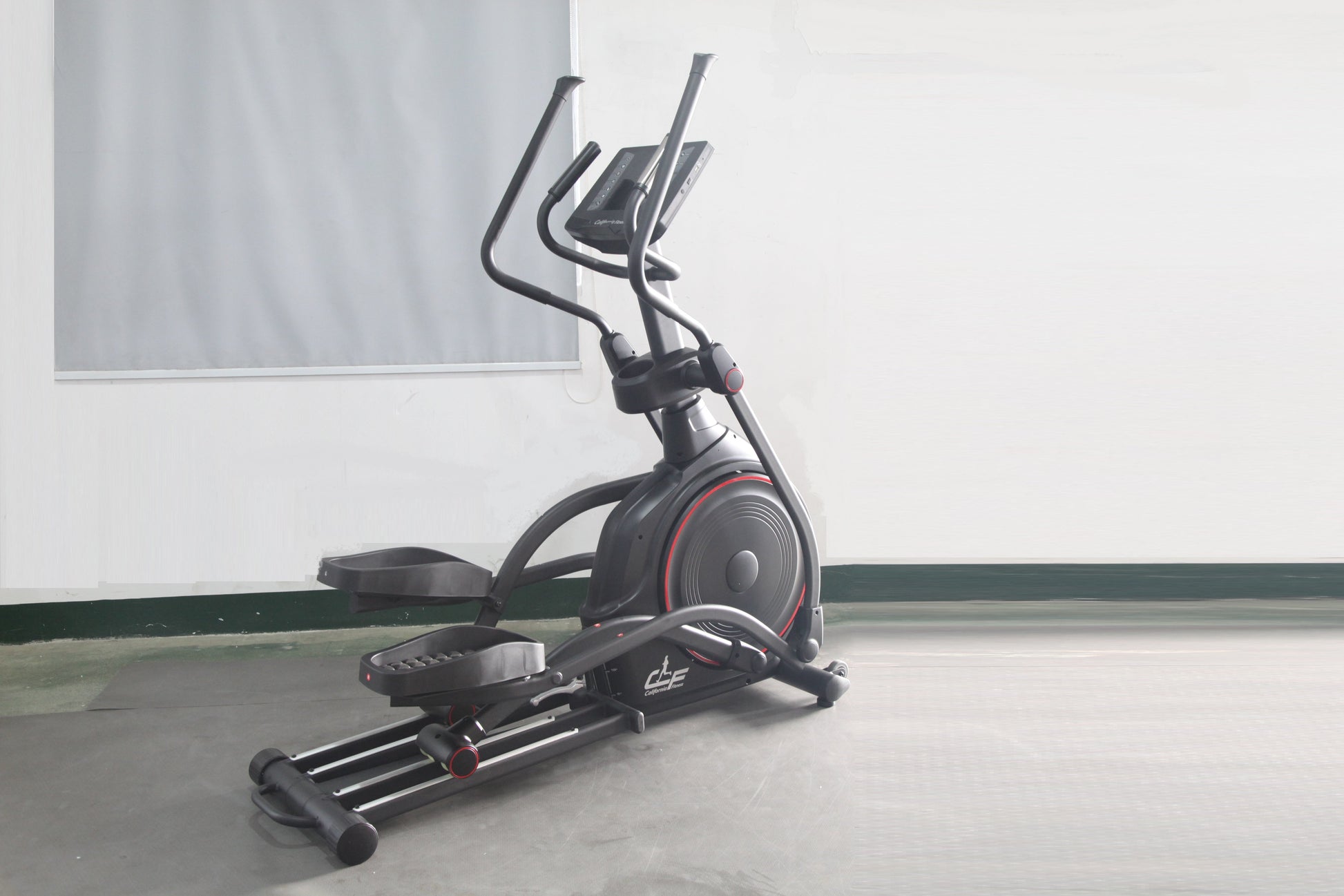 Black and red elliptical incline trainer with dual curved handles and digital display on concrete floor against white wall
