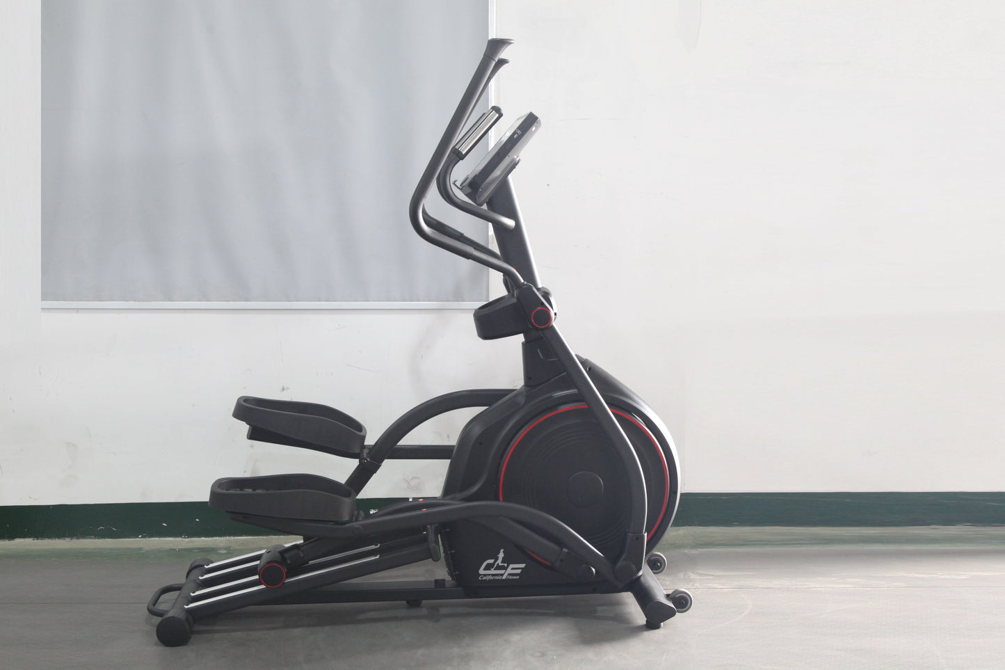 Black elliptical machine with red accents and dual handlebars, displayed on concrete floor against white wall