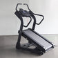 Black incline trainer treadmill with digital display console and curved handles on concrete floor against white wall