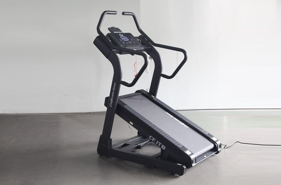 Black incline trainer treadmill with digital display console and curved handles on concrete floor against white wall