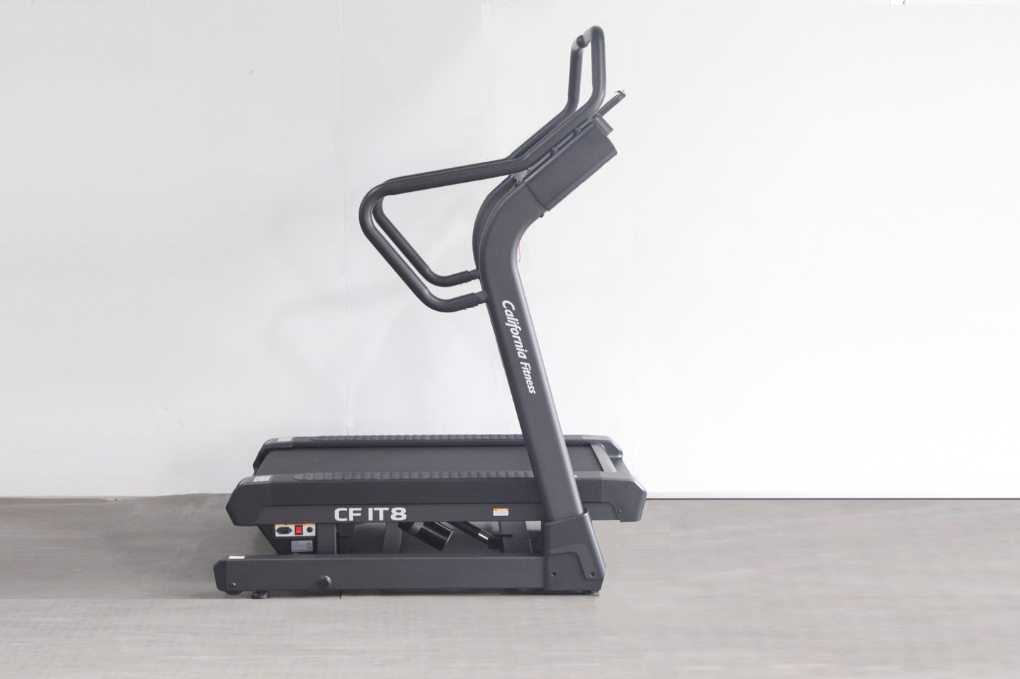 Black California Fitness IT8 incline trainer treadmill with dual handles and control panel, displayed on gray floor against w
