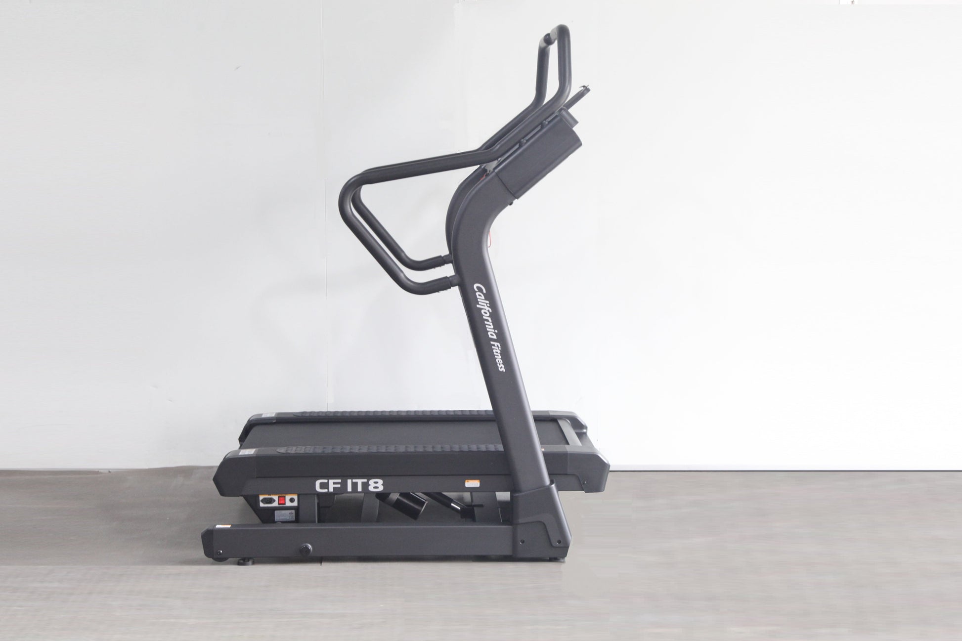 Black California Fitness IT8 incline trainer treadmill with dual handles and control panel, displayed on gray floor against w