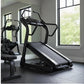 Black motorized treadmill with incline feature and curved handles in modern gym setting with large windows