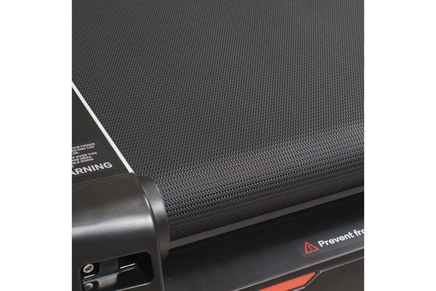 Close-up of black textured treadmill running belt with dark frame and control panel showing warning label