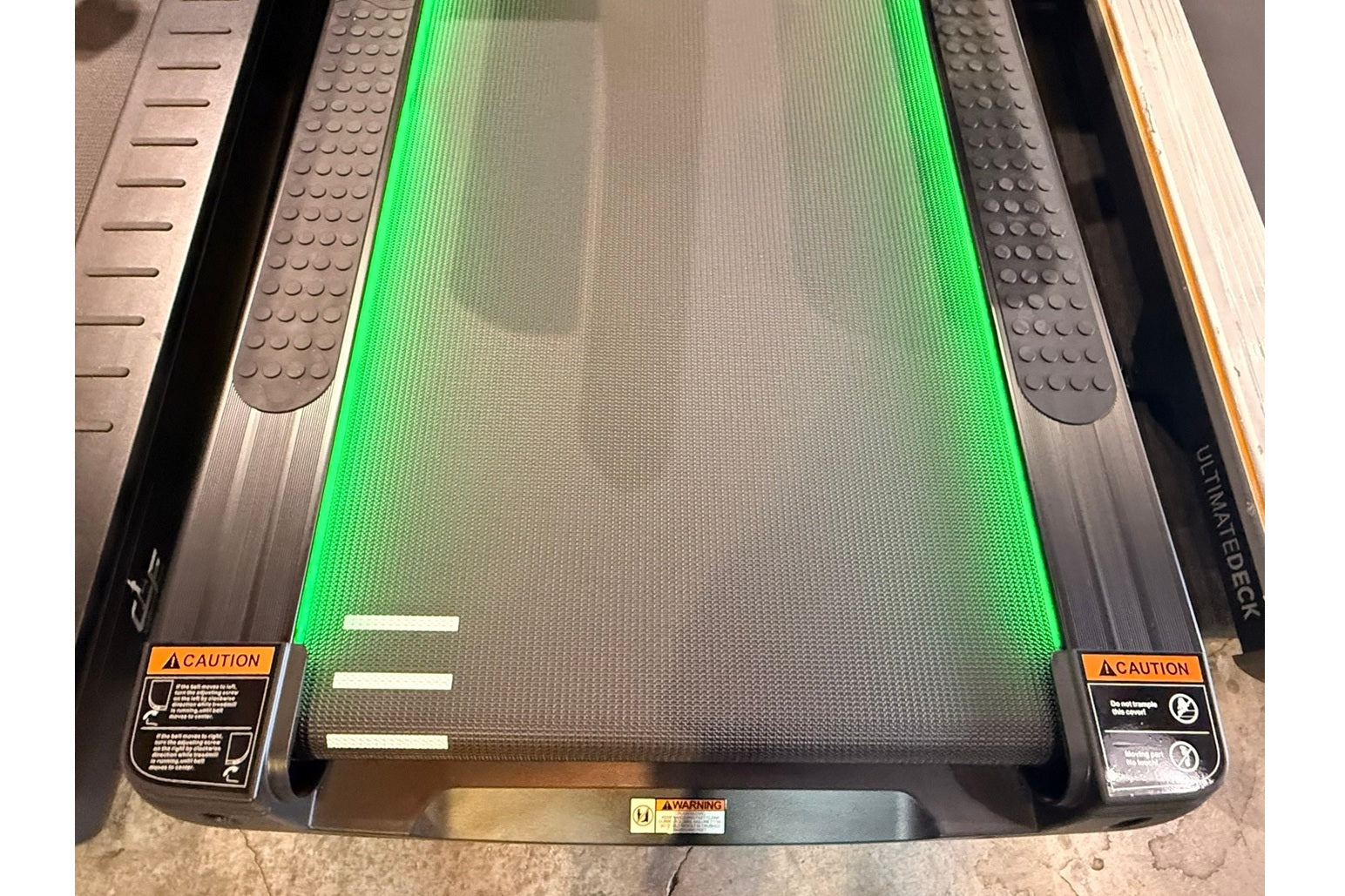 Treadmill running deck with bright green belt and gray side rails with textured grip surfaces, viewed from above
