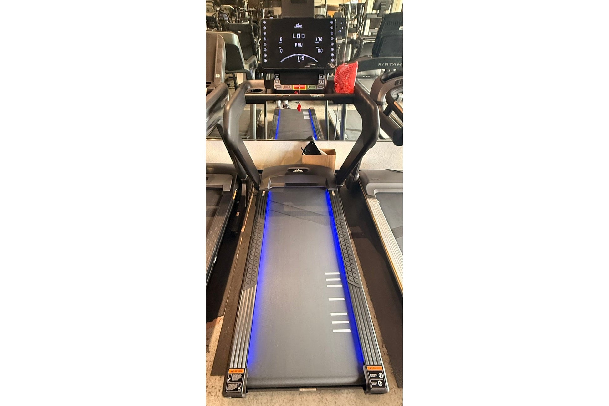 Black motorized treadmill with blue side rails, digital display console, and curved black handles, shown in showroom setting